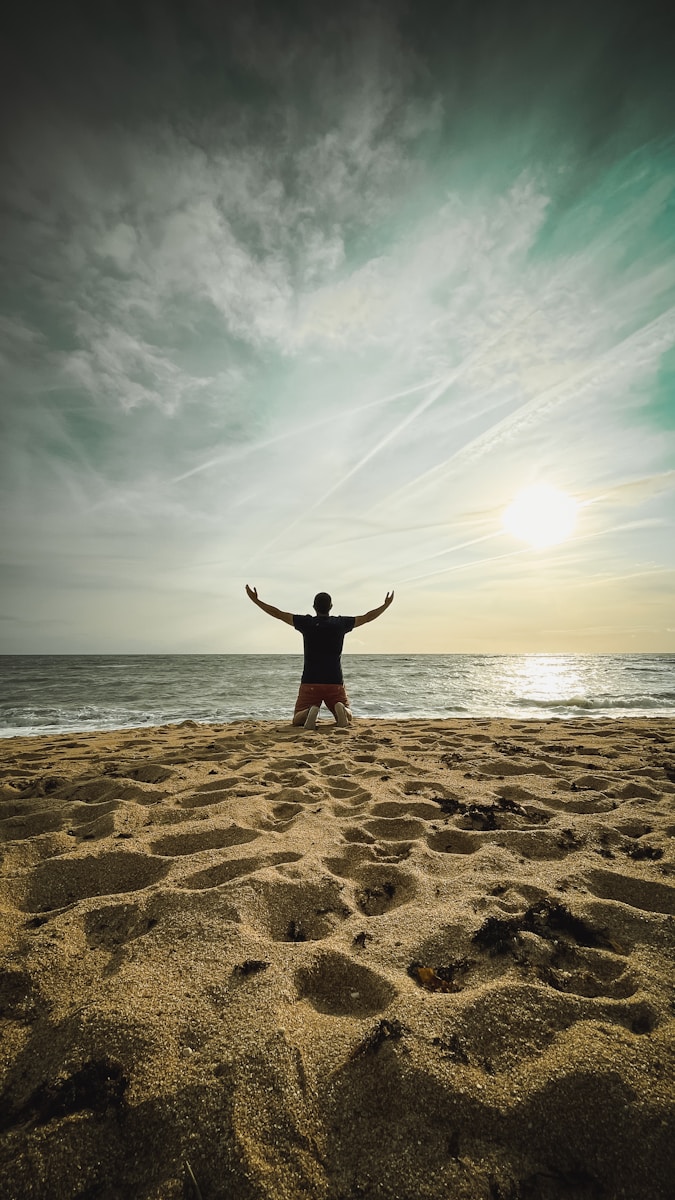 Man with arms raised on beach at sunset