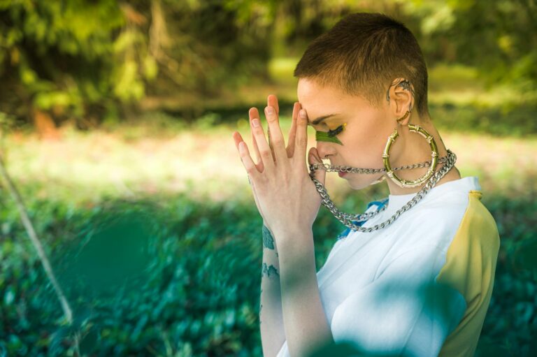 Young woman in prayer pose outside, showcasing contemporary style and spiritual connection.
