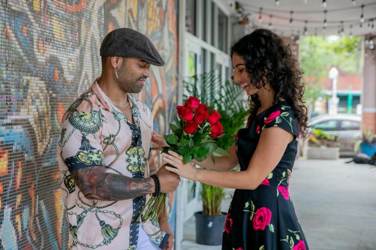 A man gives a bouquet of red roses to a smiling woman on a lively street scene.