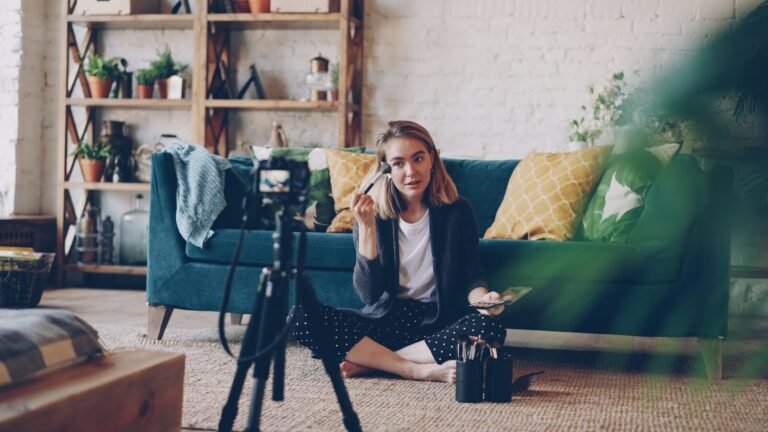 Woman applying makeup for camera in living room